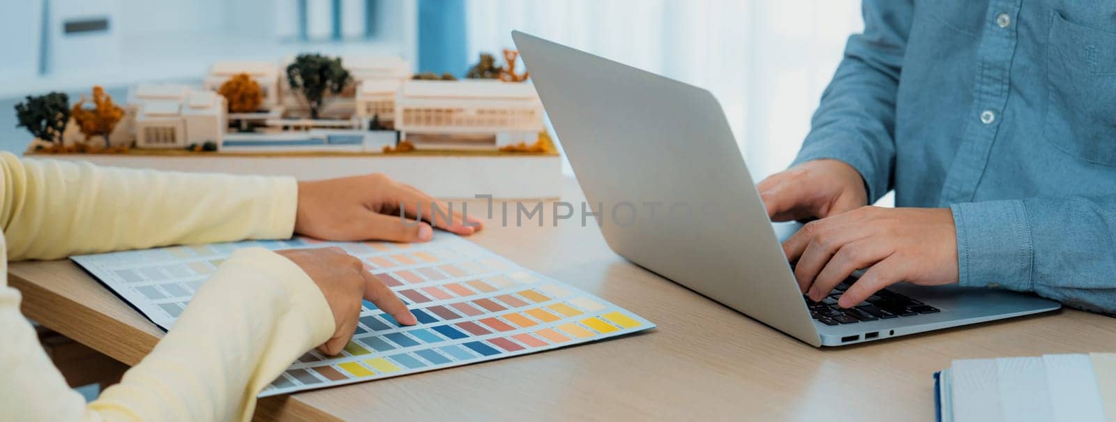 Architect interior designer selects color by using color swatches during his colleague searching information by using laptop. Creative design and teamwork concept. Closeup. Variegated.