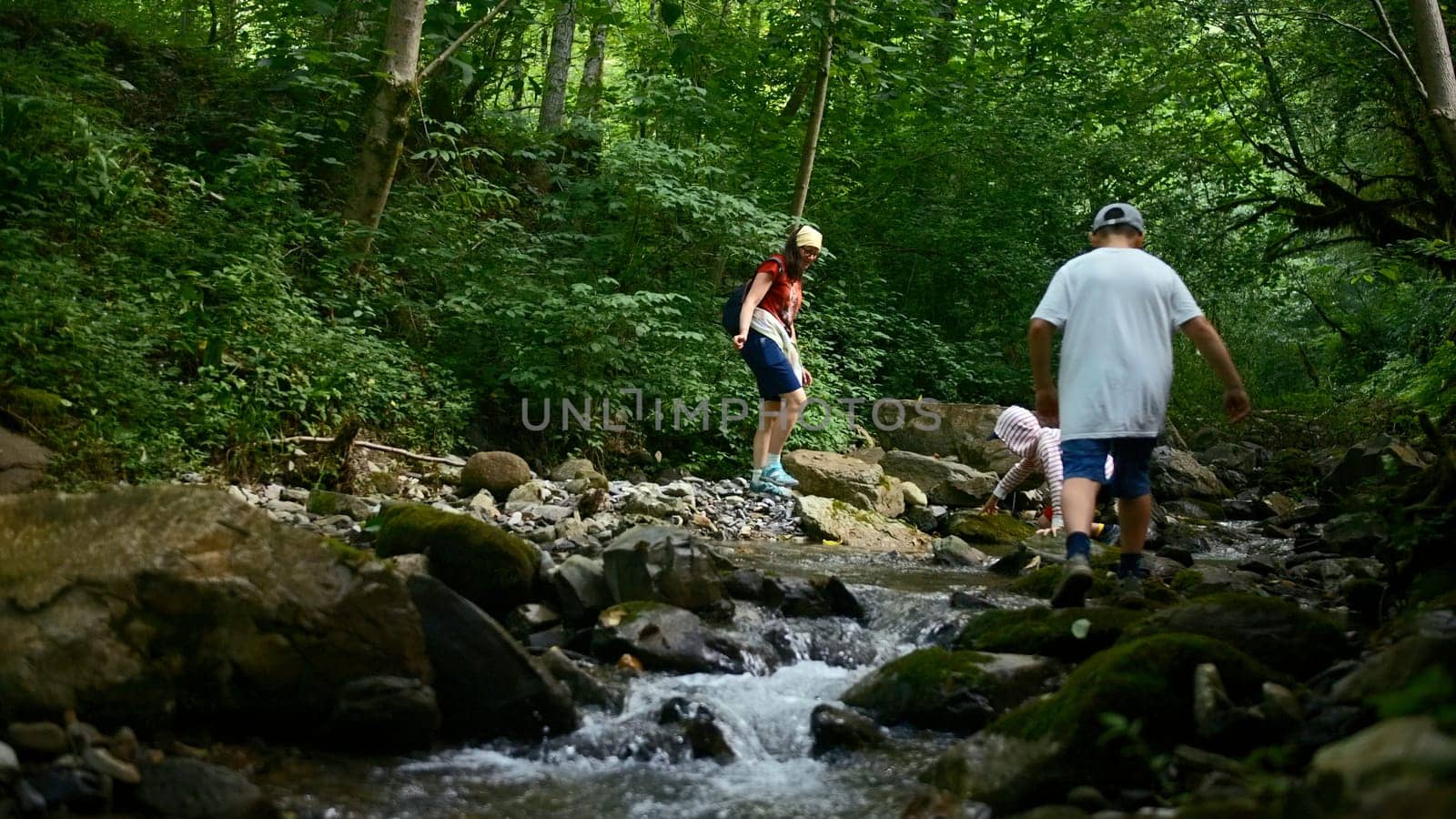 Family of mother and two boys jumping rocks across creek. Creative. Young travelers hiking together in North Carolina woods. by Mediawhalestock