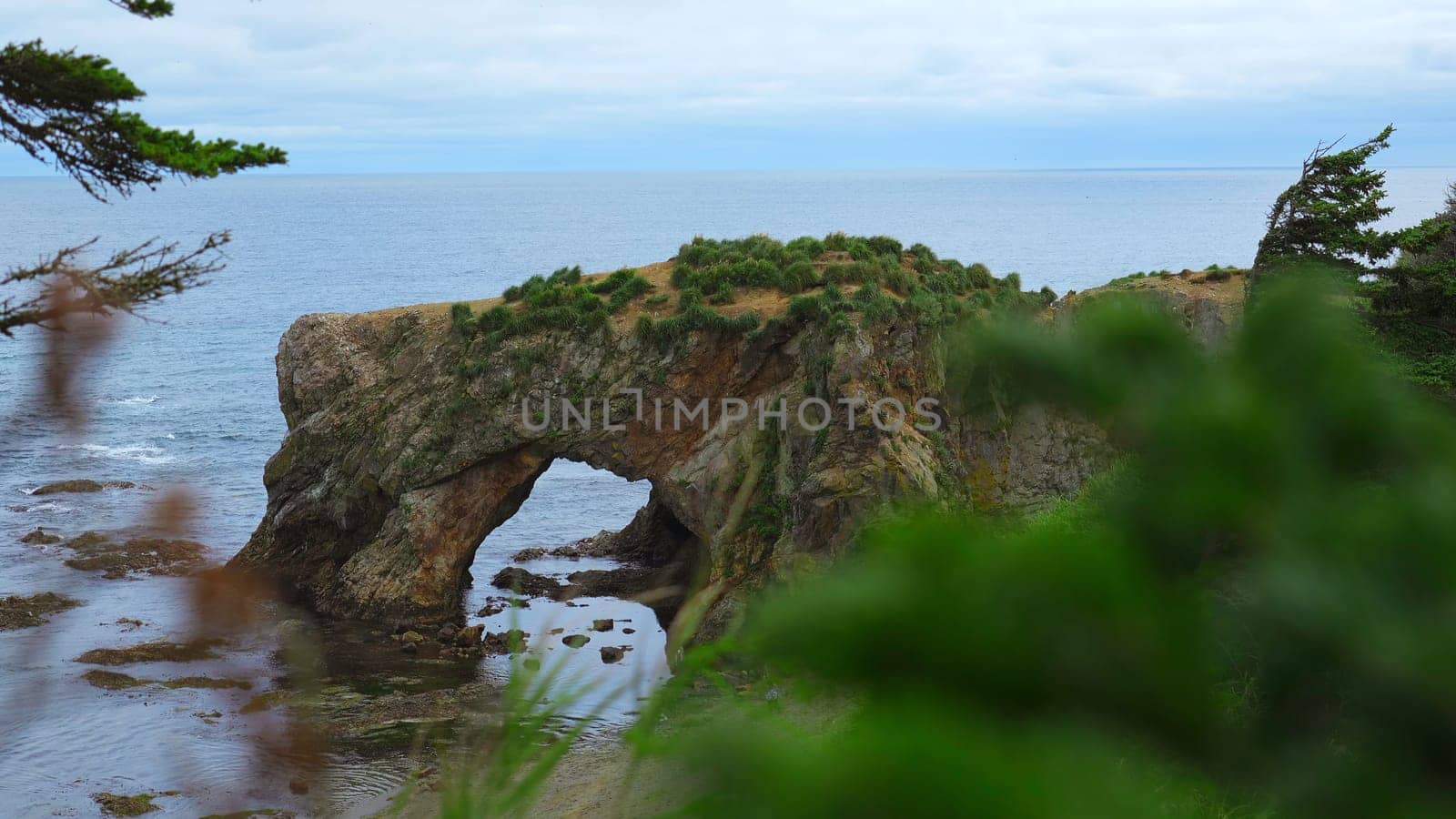 Amazing arch in rock on seashore. Clip. Beautiful seascape with rocky arch on shore. Picturesque view of rock with arch into sea on cloudy summer day.