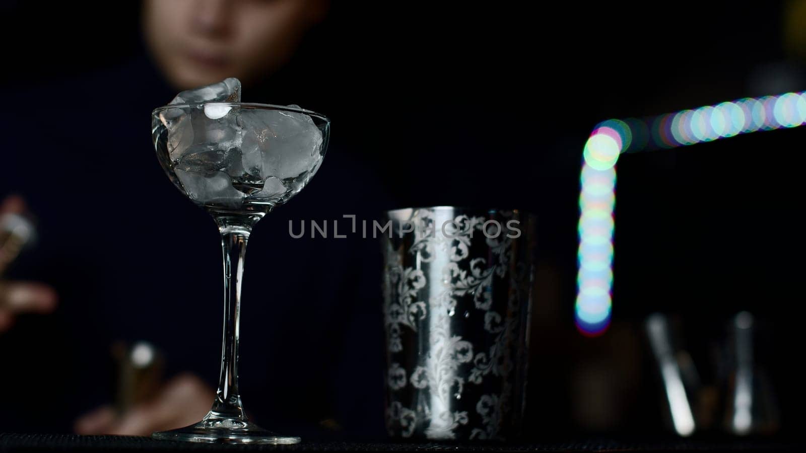 Close up of glass with ice cubes prepared for cocktail. Media. Bartender mixing alcohol liquids in a shaker