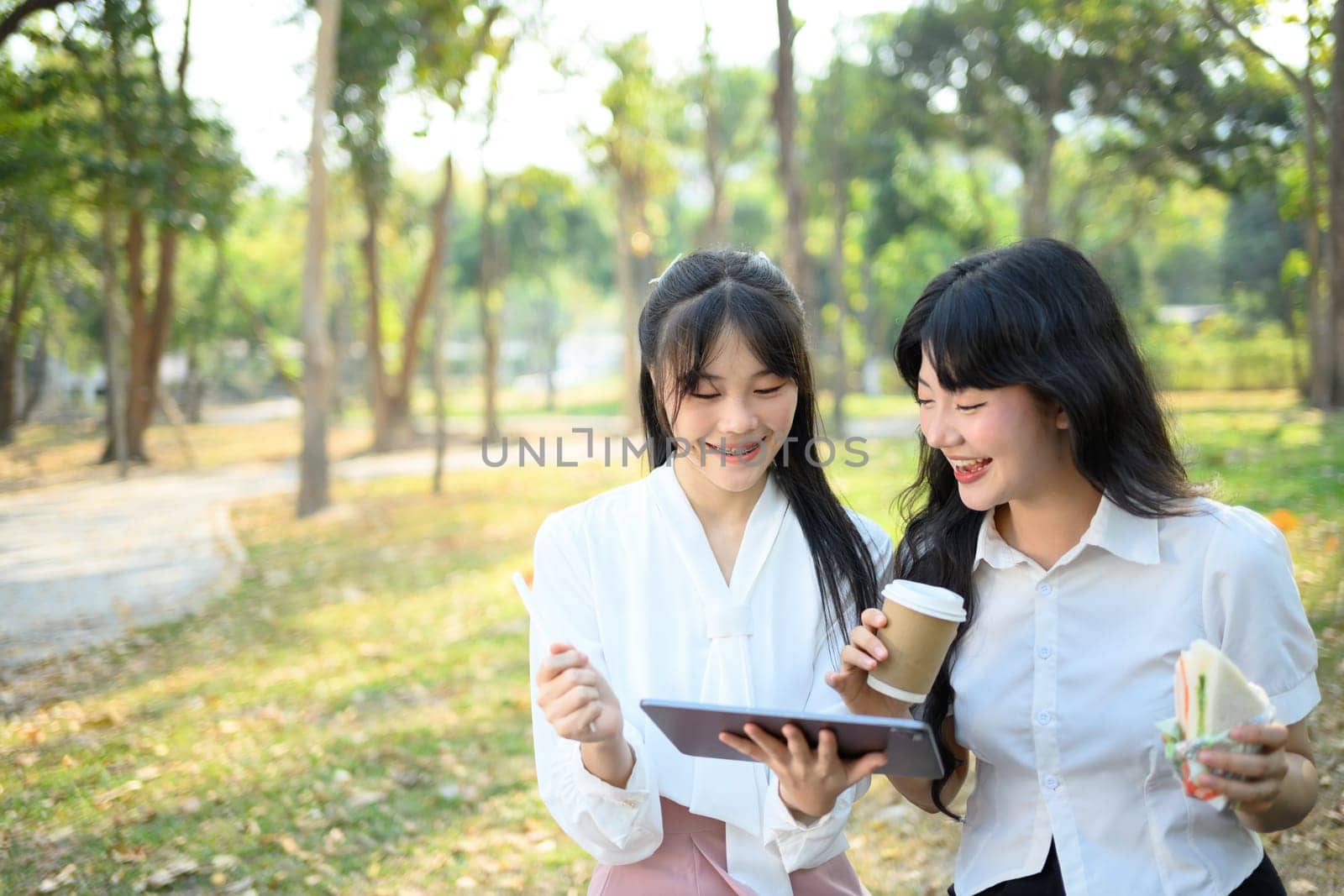 Smiling female coworkers using digital tablet and discussing project at the park by prathanchorruangsak