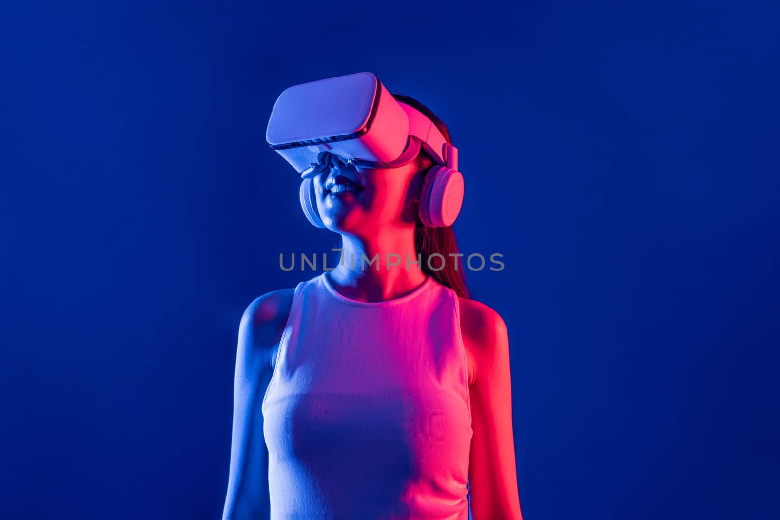 Smart female stand with surrounded by cyberpunk neon light wear VR headset connecting metaverse, futuristic cyberspace community technology. Elegant woman look generated virtual area. Hallucination.