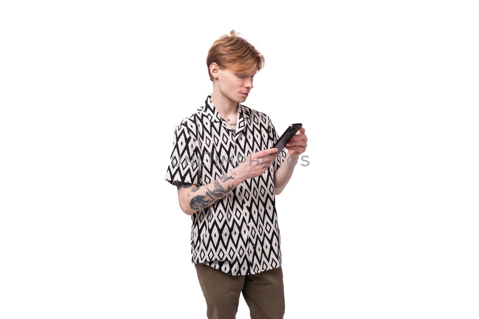 a young caucasian man with red hair and a tattoo on his arms is dressed in a stylish shirt chatting in a social network in a smartphone.