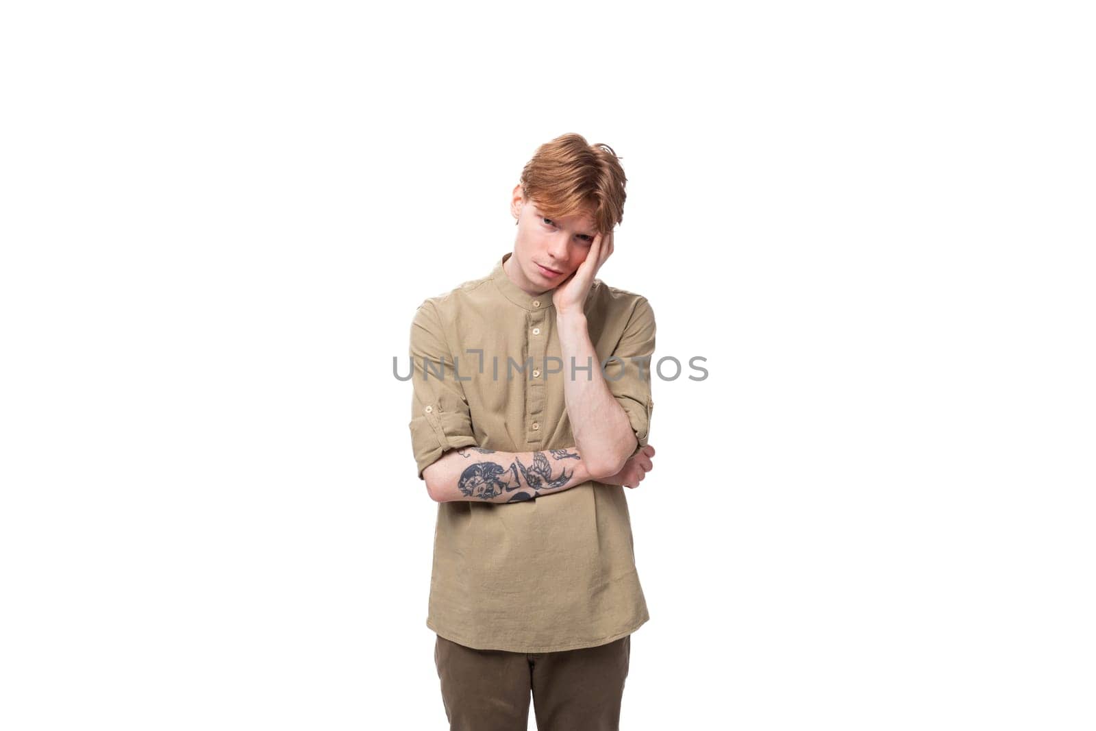 a young european guy with red hair is wearing a fashionable beige shirt and brown trousers feeling tired.