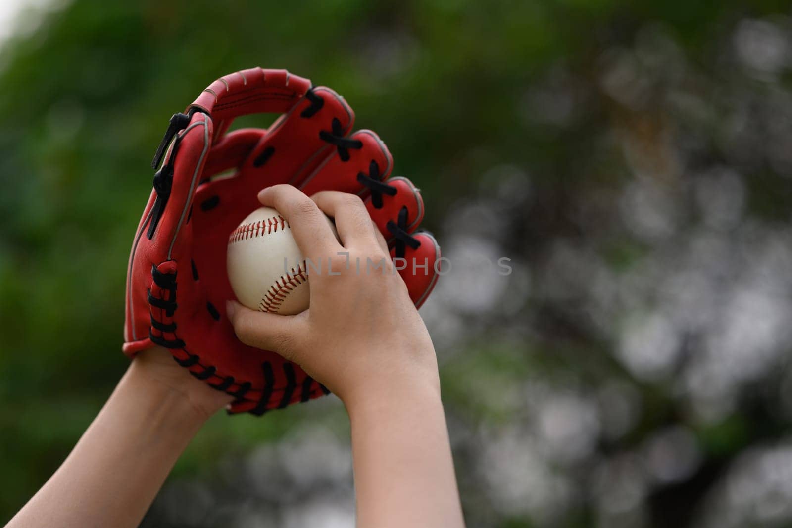 Hand of baseball player in a leather glove holding ball on blurred green background.