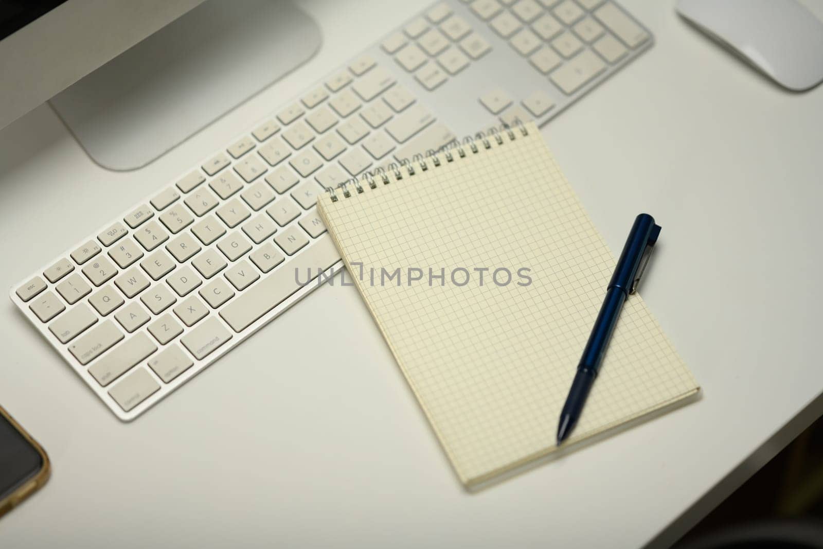 Top view of notepad, computer keyboard and mouse on white office desk.