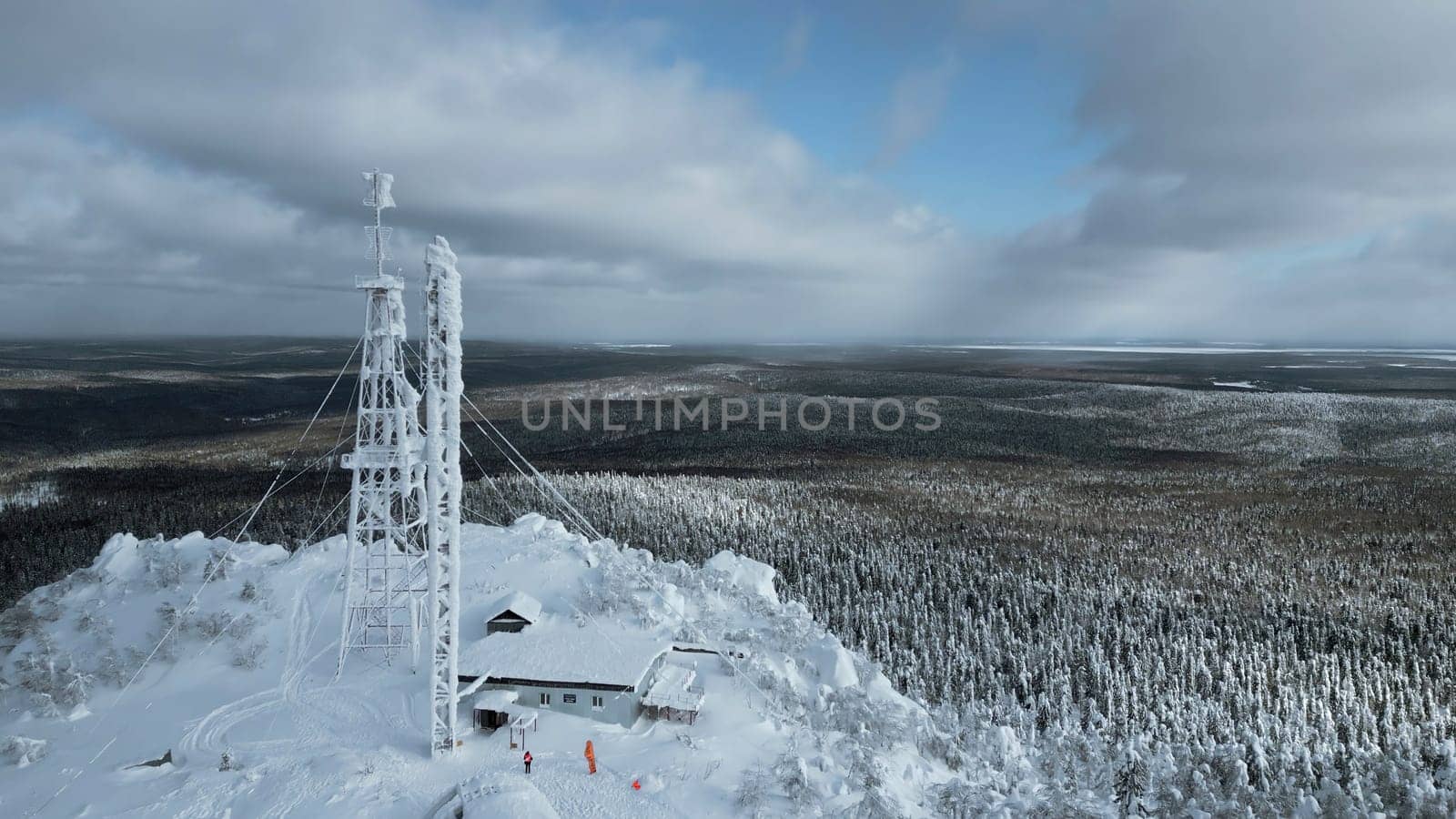 Frozen repeater antenna on the top of a hill in winter. Clip. Aerial view of winter valley panorama and blue cloudy sky. by Mediawhalestock