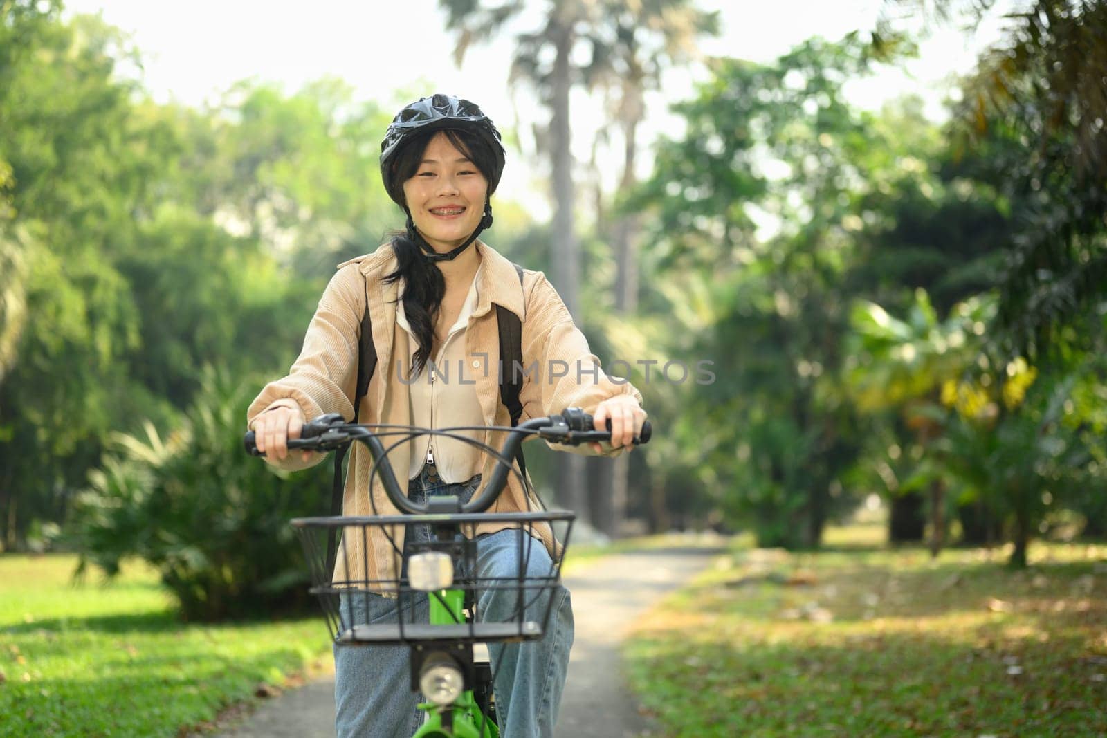 Portrait of cheerful Asian woman wearing helmet riding bicycle in the city park.