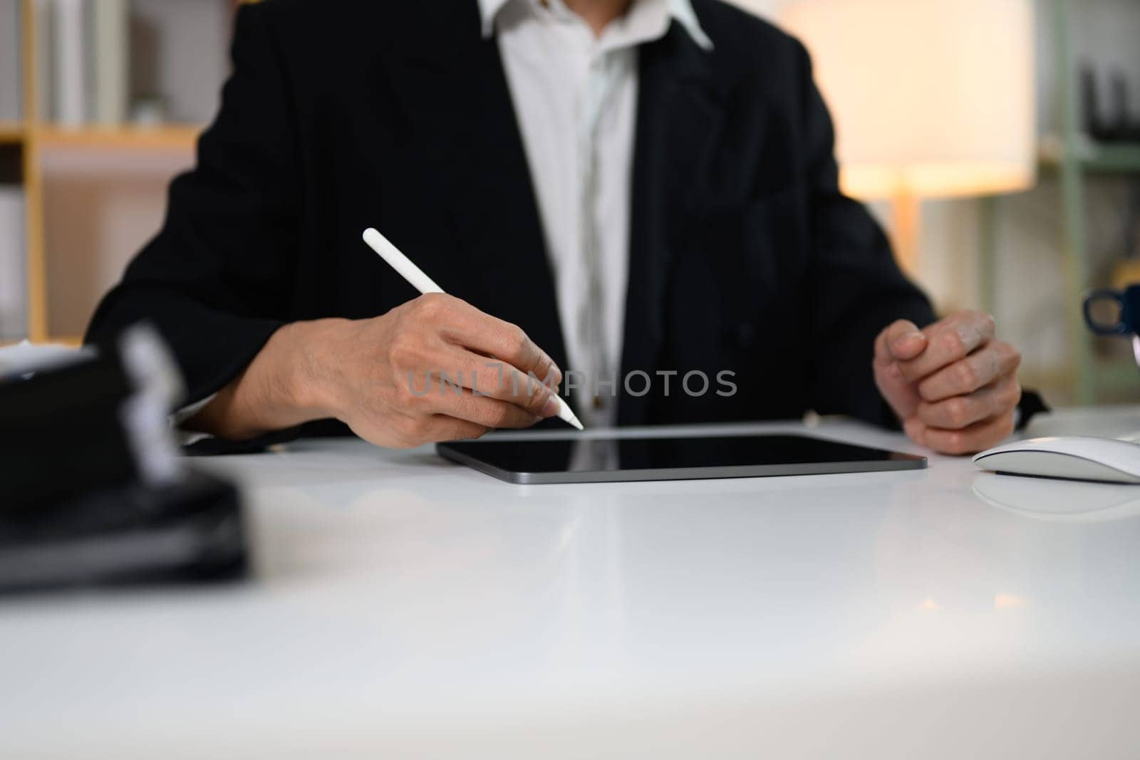 Male entrepreneur in black suit working with digital tablet at office desk.