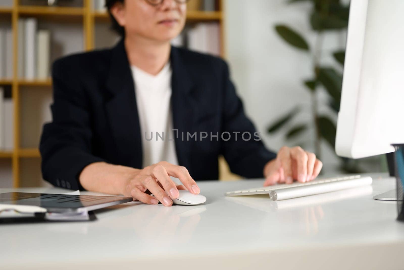 Cropped shot of senior businessman typing on keyboard and scrolling mouse at working desk.