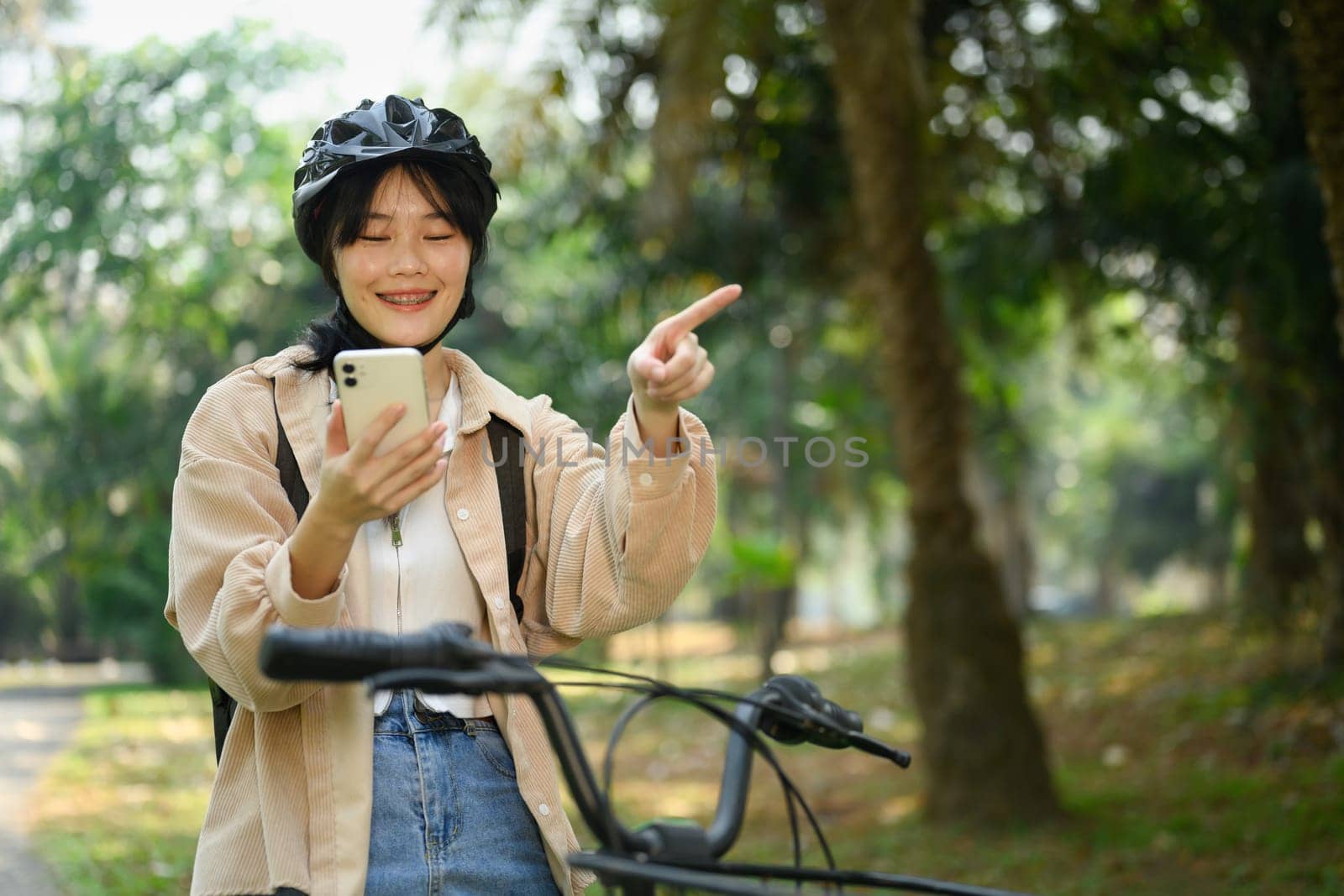 Smiling young woman riding an electric bicycle and using mobile phone for direction by prathanchorruangsak