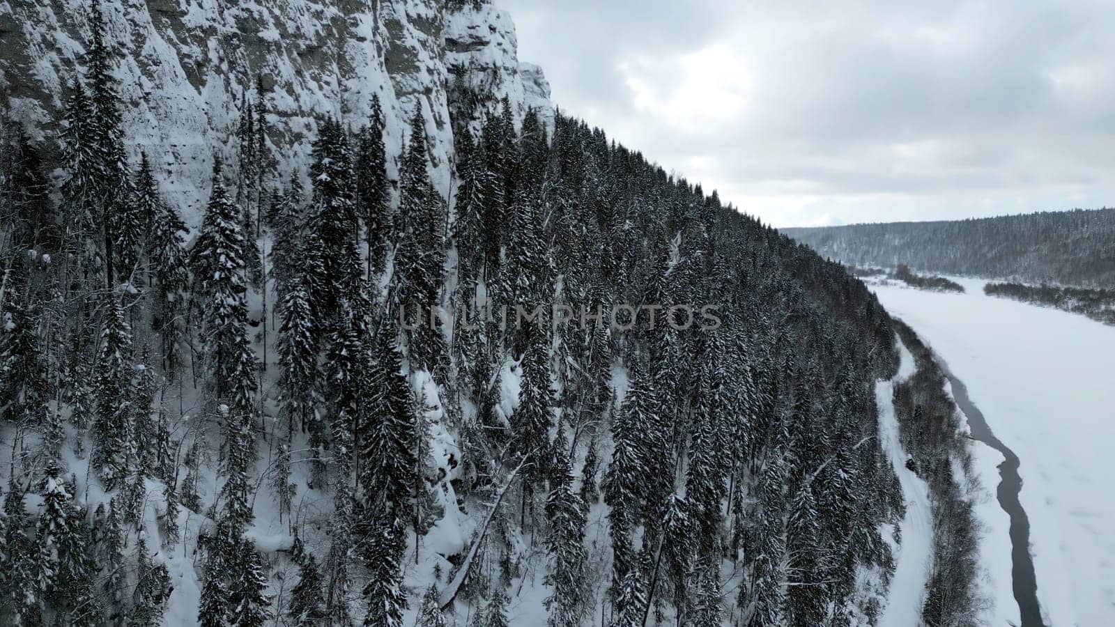 Winter mountain cliff covered by snow, ice, and fur trees. Clip. Stunning frozen winter nature, aerial view. by Mediawhalestock
