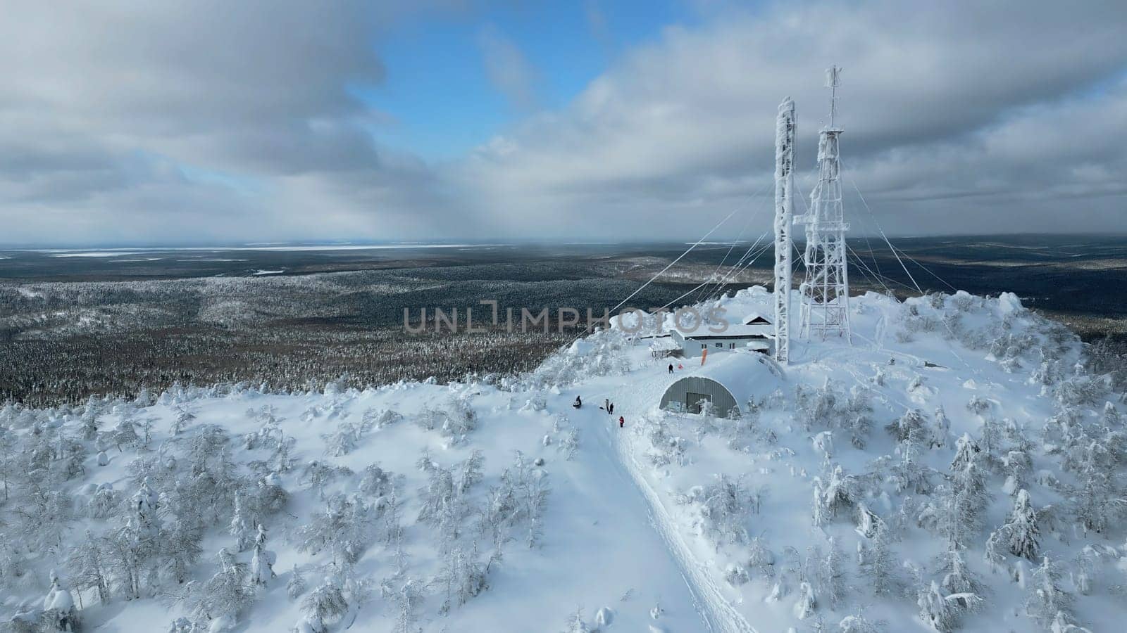 A flight over the dense winter Siberian forest in the afternoon. Clip. White mountain and a frozen weather tower on its top