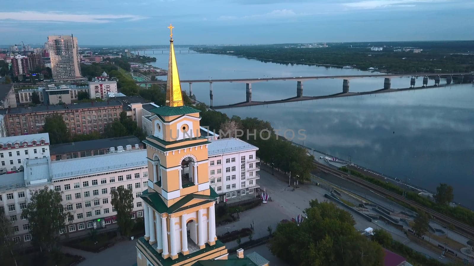 Top view of beautiful city church on river bank with bridge. Clip. Beautiful urban landscape with temple on riverbank on cloudy day. City with church on river with bridge.