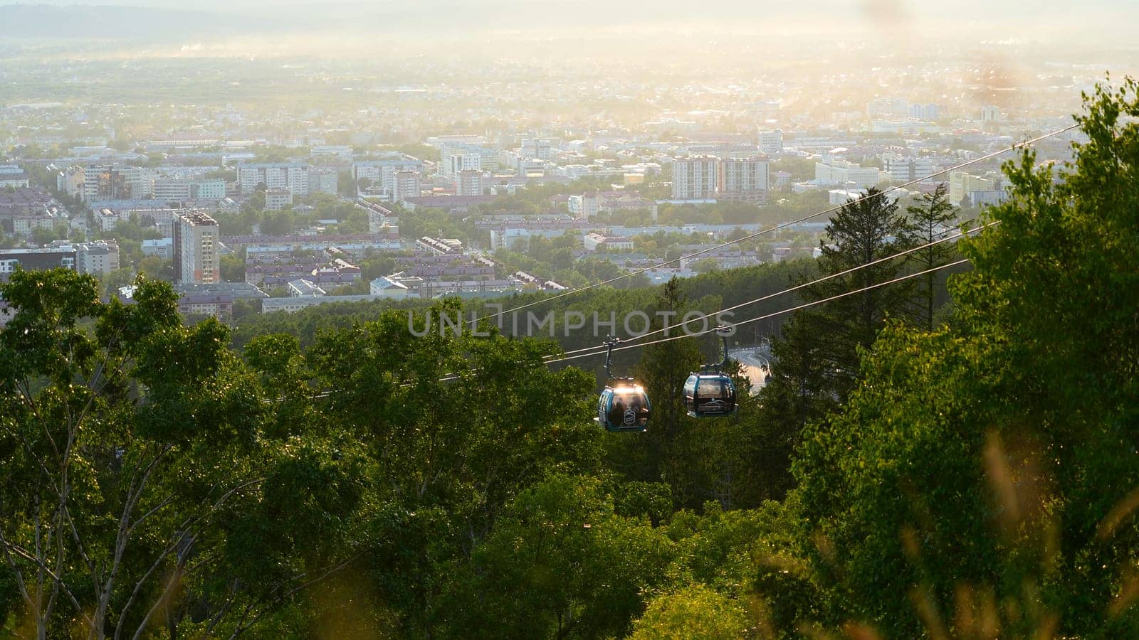 Beautiful view of cable car with view of town in summer. Clip. Green forest on slope with moving cable ways on edge of town. Beautiful city in valley with cable car on sunny summer day by Mediawhalestock