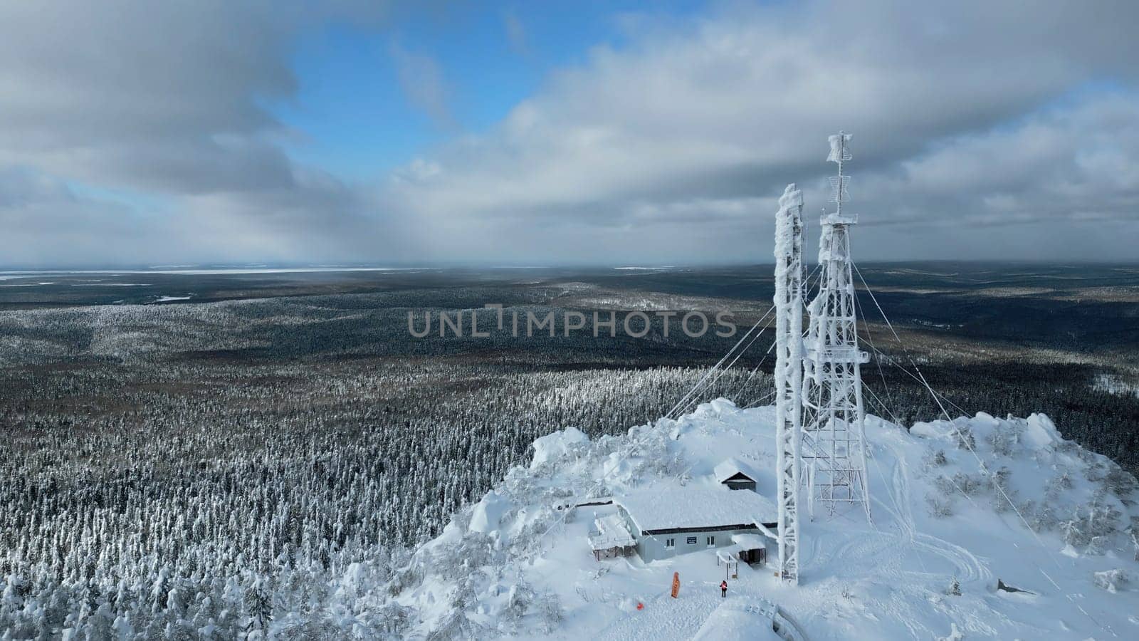 Frozen repeater antenna on the top of a hill in winter. Clip. Aerial view of winter valley panorama and blue cloudy sky. by Mediawhalestock