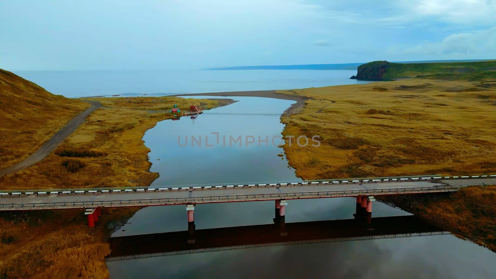 Aerial view of gorgeous nature a bridge between the river shores. Clip. Rural landscape with golden agricultural fields around and the sea shore