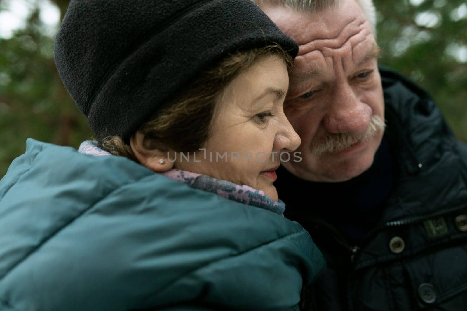 Cute retired couple walking in the park and hugging each other in winter park.