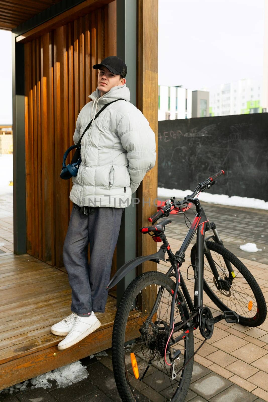 A man in a cap and a warm jacket stands with a rental bicycle.
