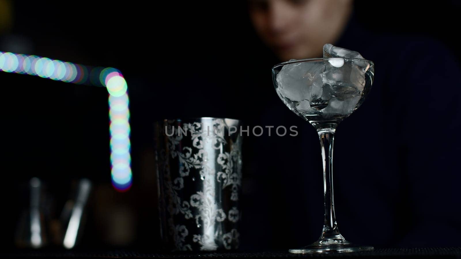 Close up of glass with ice cubes prepared for cocktail. Media. Bartender mixing alcohol liquids in a shaker