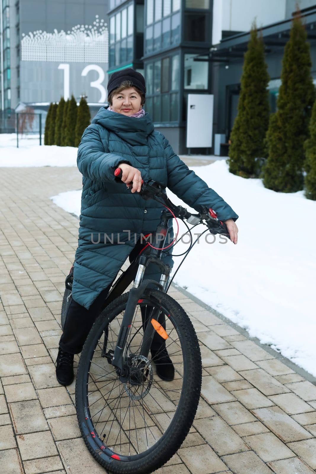 Mature European woman dressed in a winter coat rides a bicycle along the city streets by TRMK
