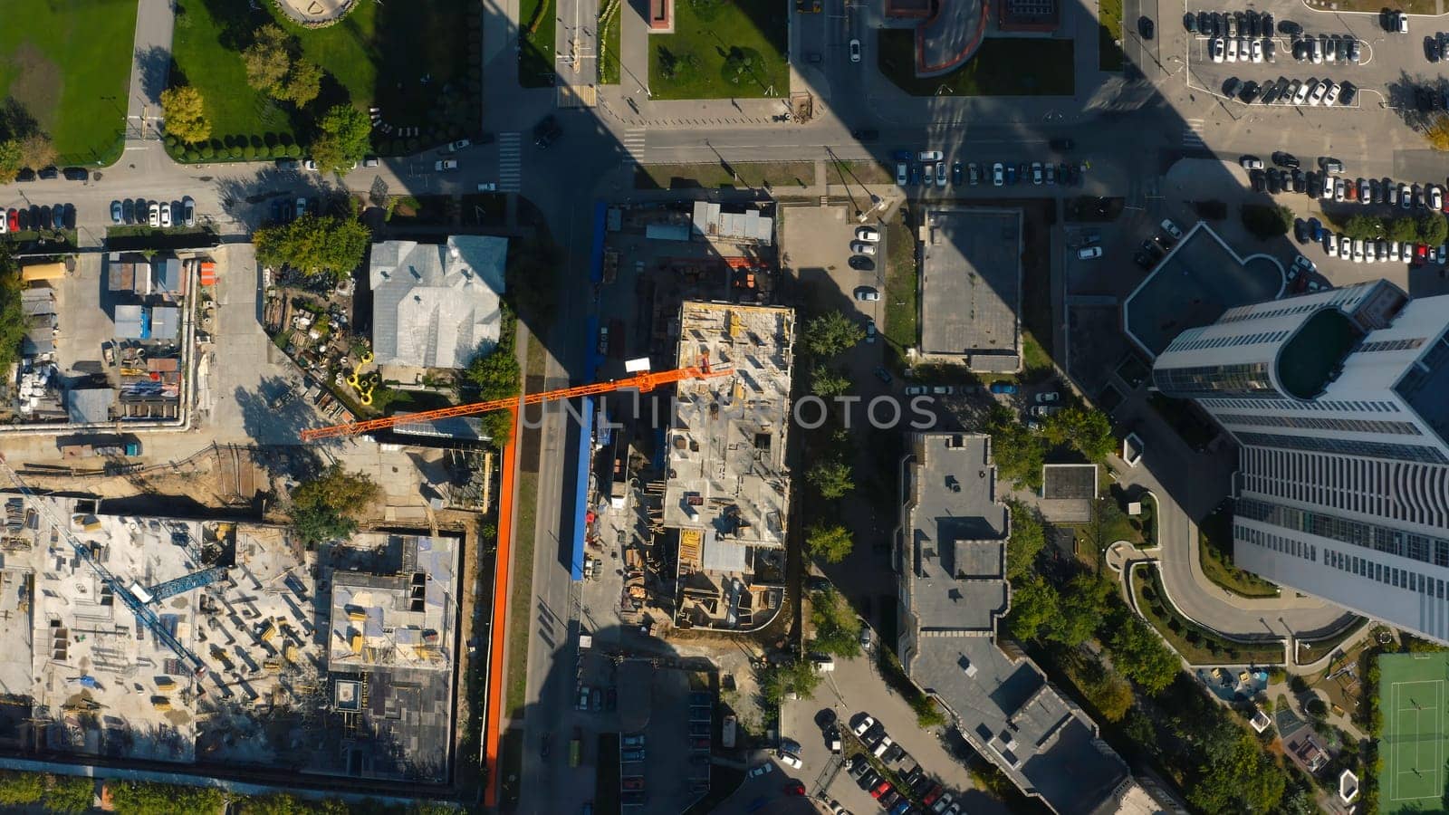 Vertical top view of construction crane in city. Stock footage. Building under construction in center of modern city on sunny summer day. Construction crane in city center.