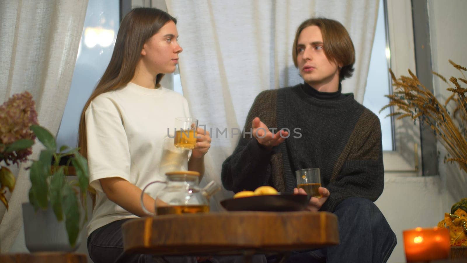 Young man and woman are talking over tea in cafe. Media. Young couple of students are talking with tea in cozy cafe. Couple on student break with tea and comfortable conversation by Mediawhalestock