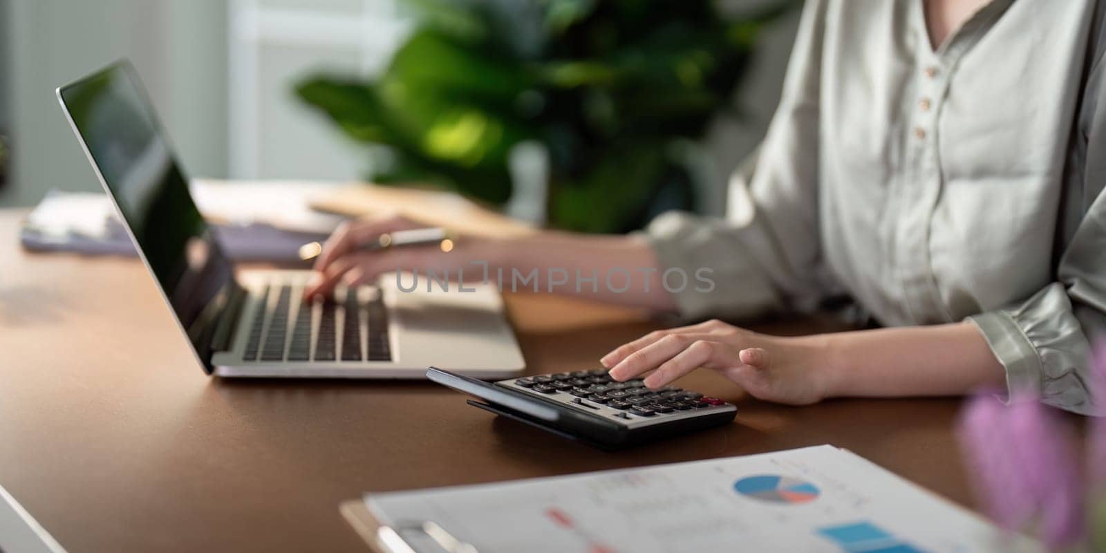 Businesswoman using laptop computer and working at office with calculator document on desk, doing planning analyzing the financial report, business plan investment, finance analysis concept.