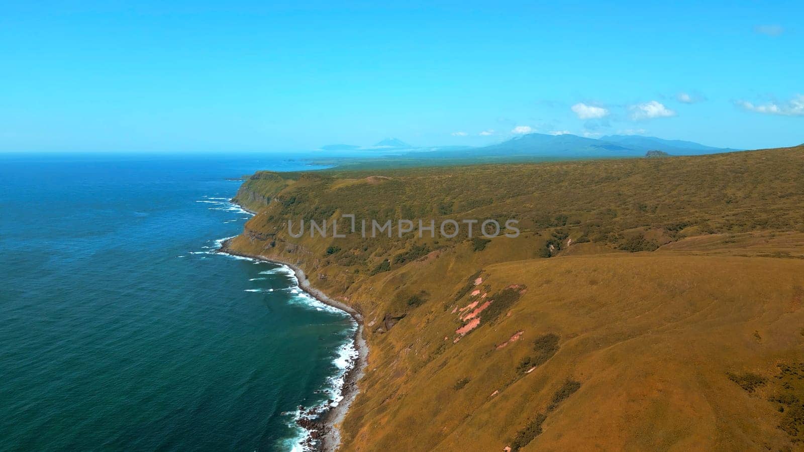 Autumn sunny day on the shore with smooth sea waves. Clip. Aerial view of hills covered by withered grass and dark blue sea. by Mediawhalestock