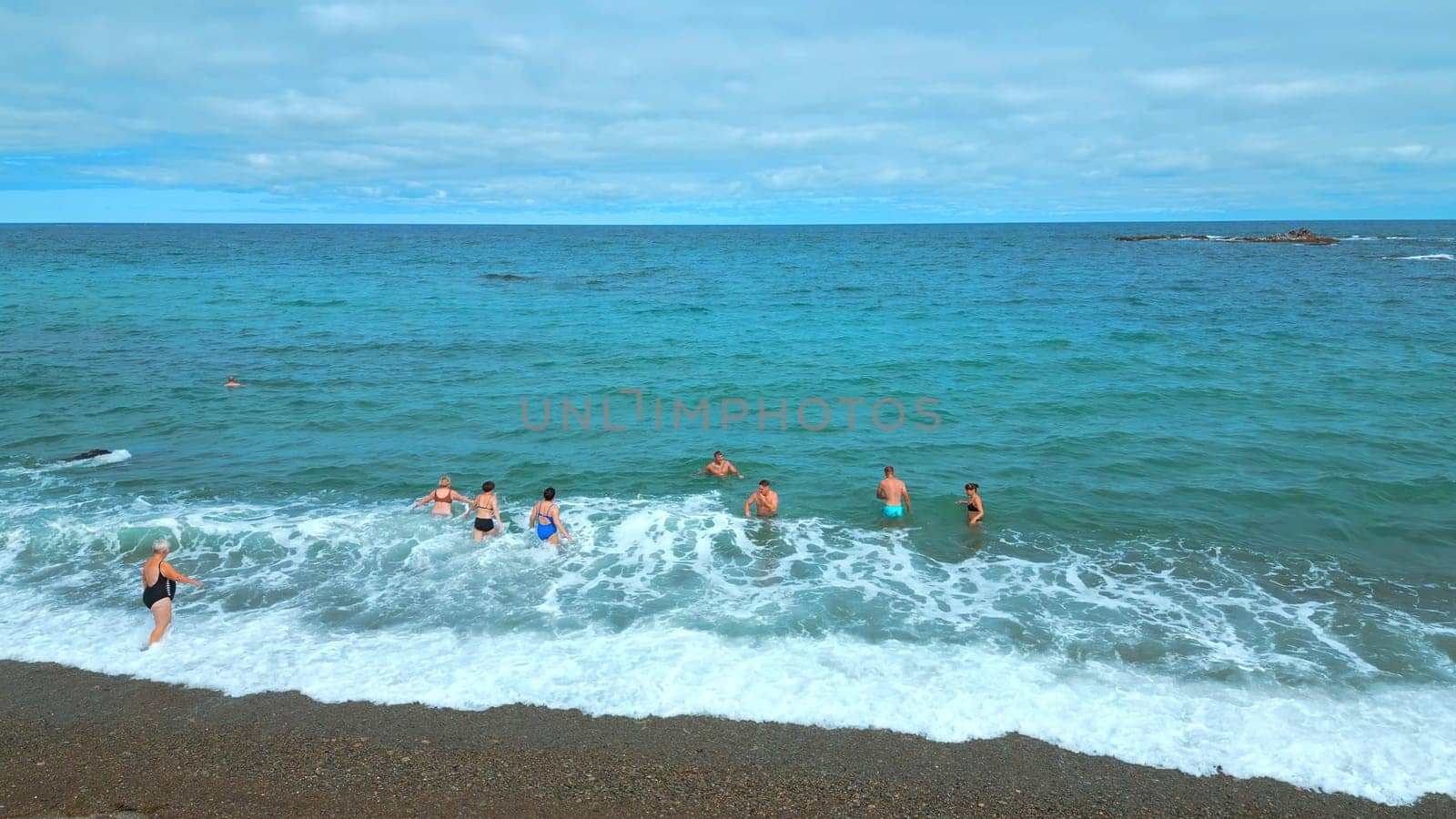 Top view of people swimming in blue water on cloudy day. Clip. Beautiful blue sea with waves and floating people. Tourists swim and relax on beautiful sea with blue water by Mediawhalestock