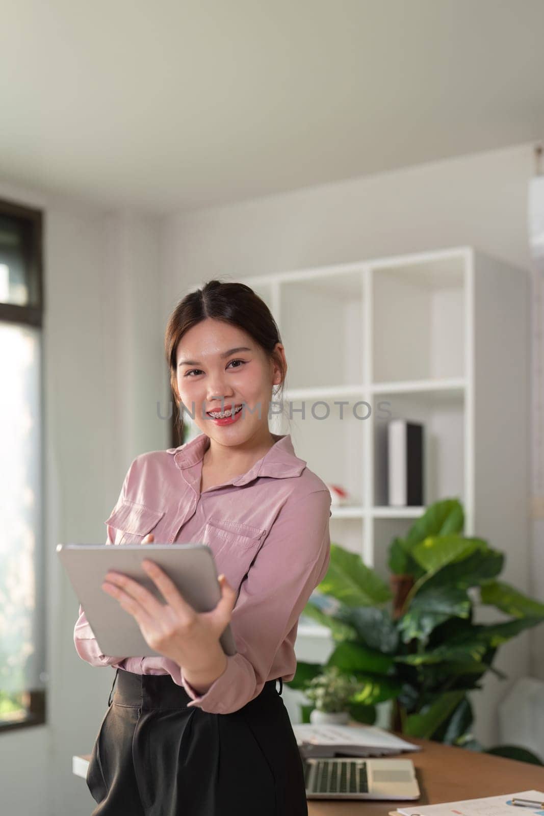 Young smiling successful employee business woman work use hold tablet stand at workplace desk at home office . Achievement career concept by nateemee