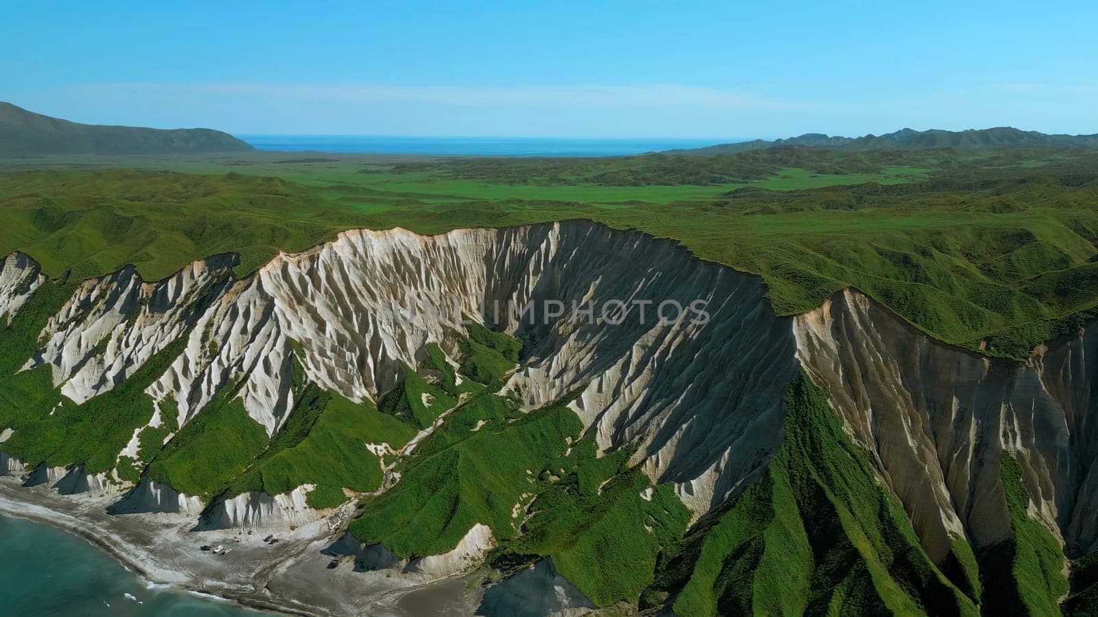 Green slopes meeting blue ocean aerial view. Clip. White cliffs and blue shore against clear blue sky