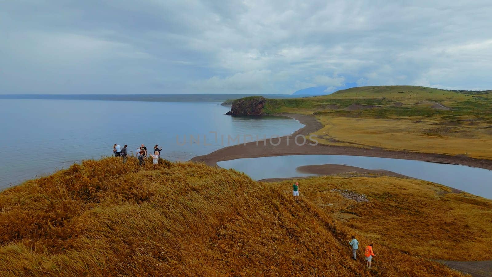 Concept of tourism, group of people on the hill top. Clip. Aerial view of yellow grass and the sea shore. by Mediawhalestock