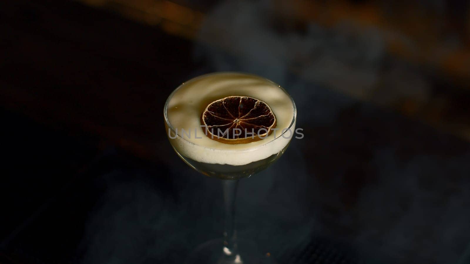 Close up of beautiful cocktail with thick foam and dried orange slice. Media. Beverage on bar counter background