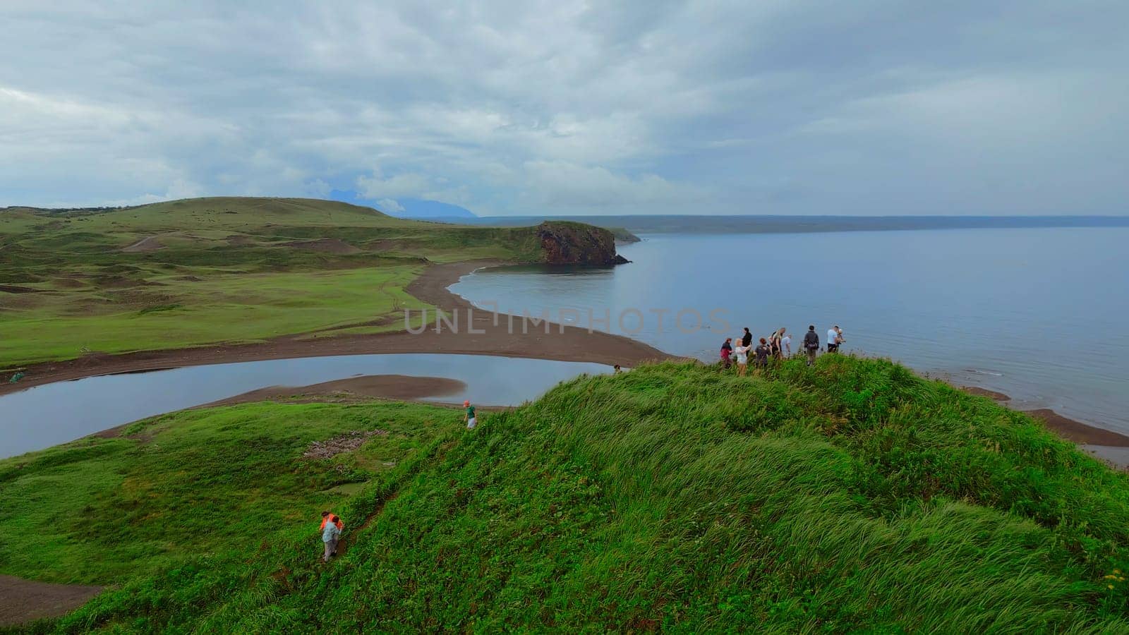 Concept of tourism, group of people on the hill top. Clip. Aerial view of green grass and the sea shore