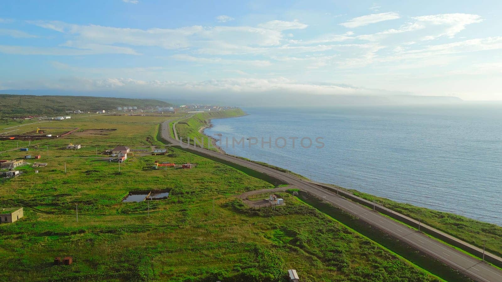 Top view of village with road to sea coast. Clip. Seascape of coast with road and village on sunny summer day. Beautiful view of coast with village and sea sunny horizon.