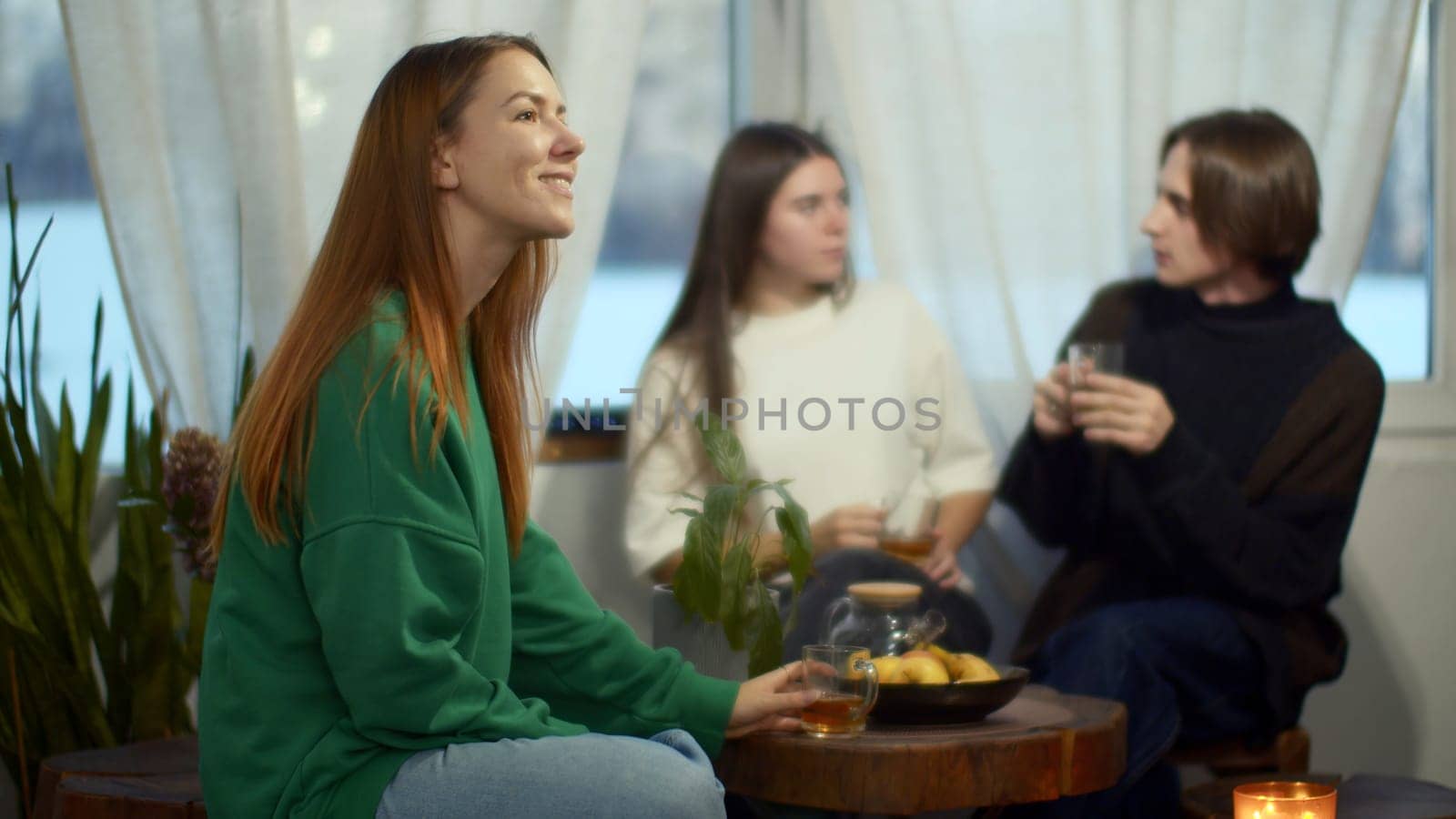 Side view of a happy relaxed woman enjoying tea and looking dreamy. Media. Blurred couple communicating on the background