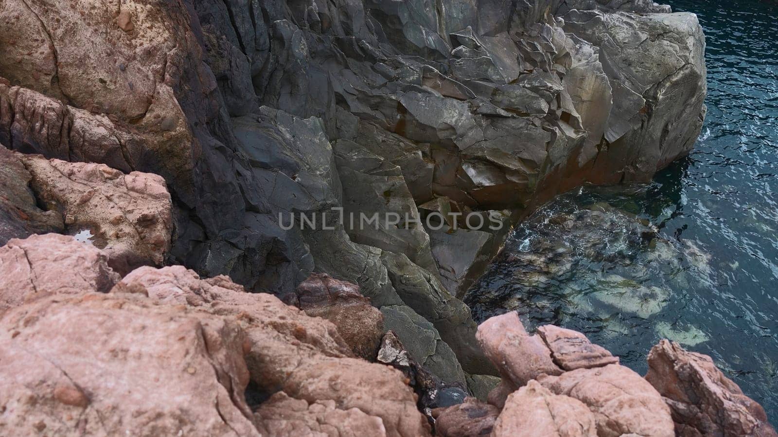 View of dangerous stone cliffs near sea water. Clip. On edge of dizzying cliffs by sea water. Beautiful and dangerous sharp rocks with sea water.