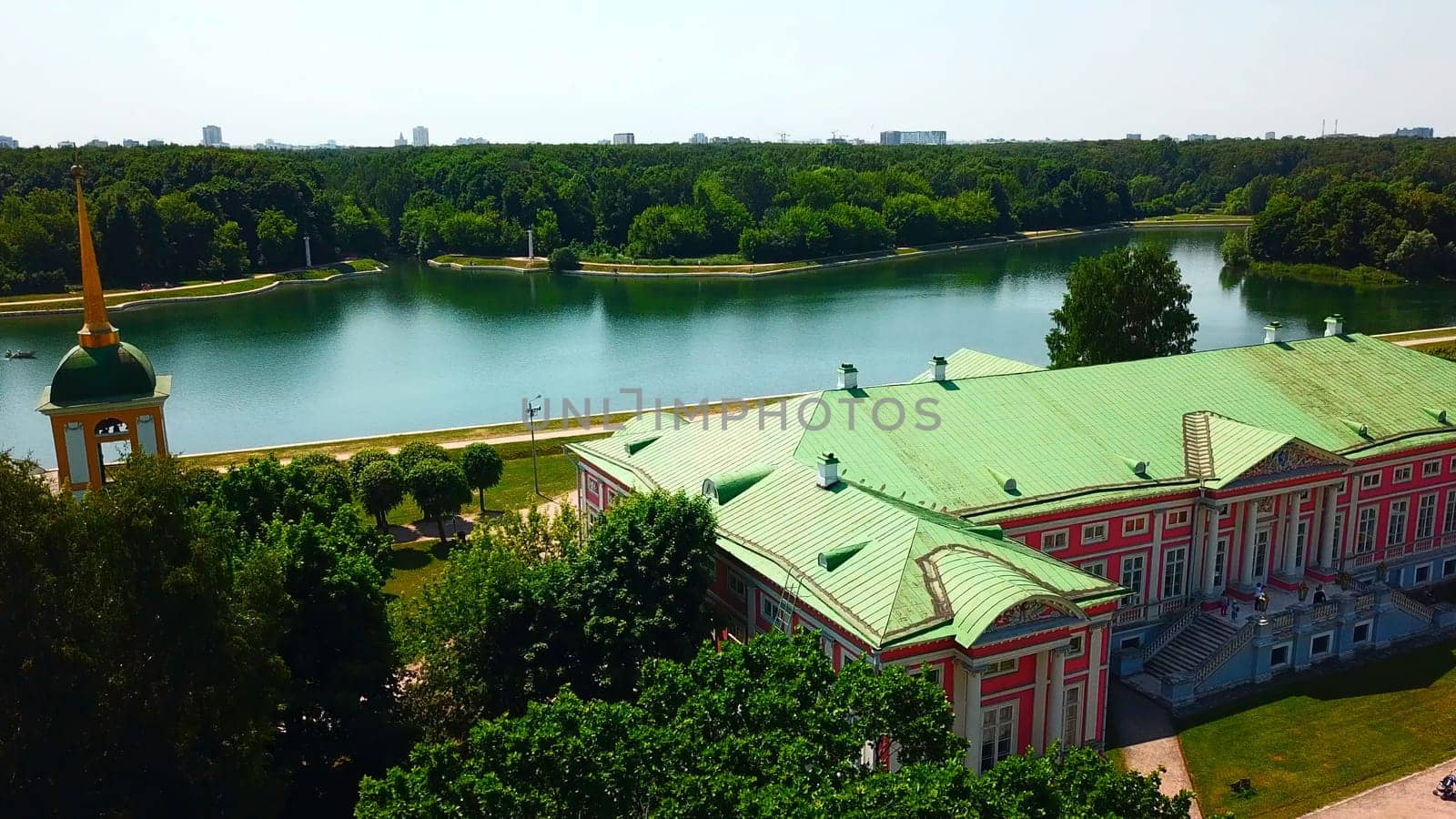 Top view of historic building by river with forest. Creative. Beautiful historical suburb with tourists on riverbank. Picturesque estate on river bank with forest on sunny summer day.