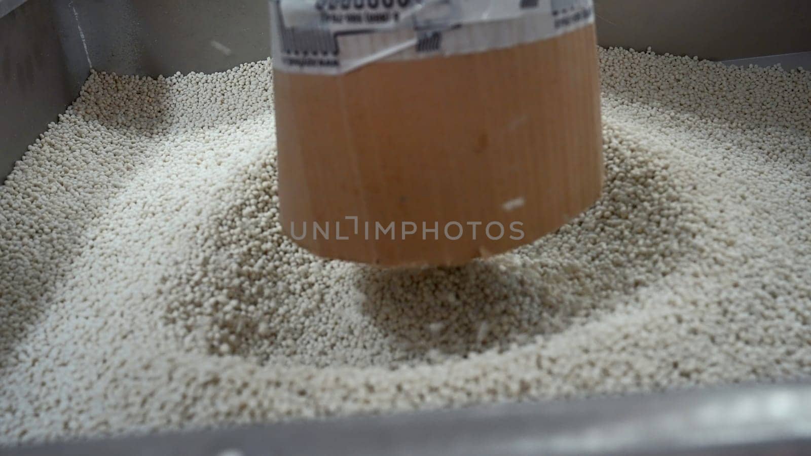Close-up of polymer granules in production. Creative. Process of extrusion and drying of plastic granules. Pile of white plastic pellets in industrial workshop.