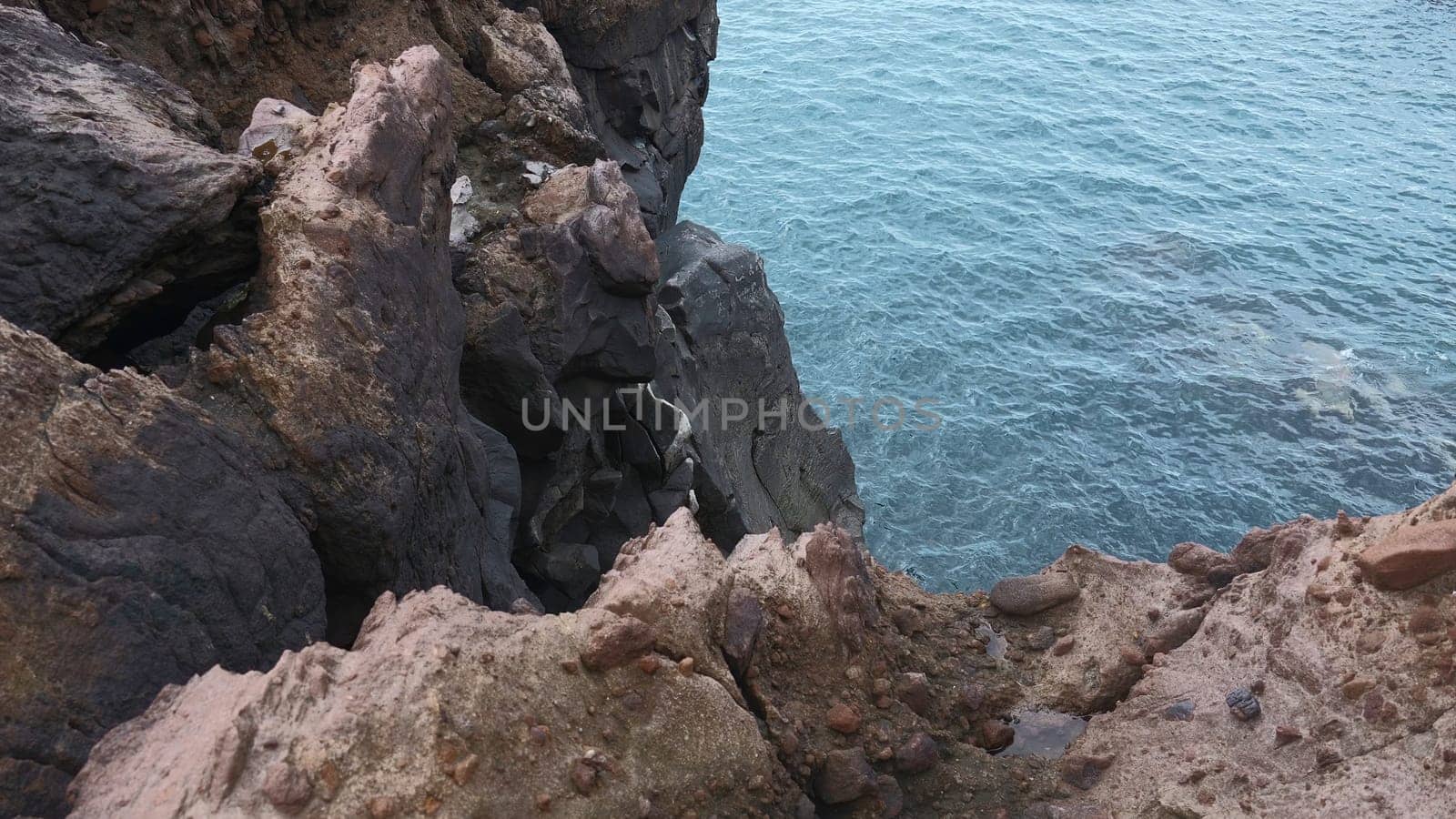 Beautiful rocks by water. Clip. Stone cliffs of coast with quiet sea water. View from edge of stone shore to sea water.