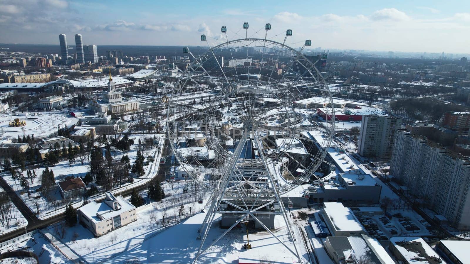 Top view of big Ferris wheel in winter. Creative. Beautiful urban landscape with Ferris wheel in city center in winter. Ferris wheel in center of big city on sunny winter day.