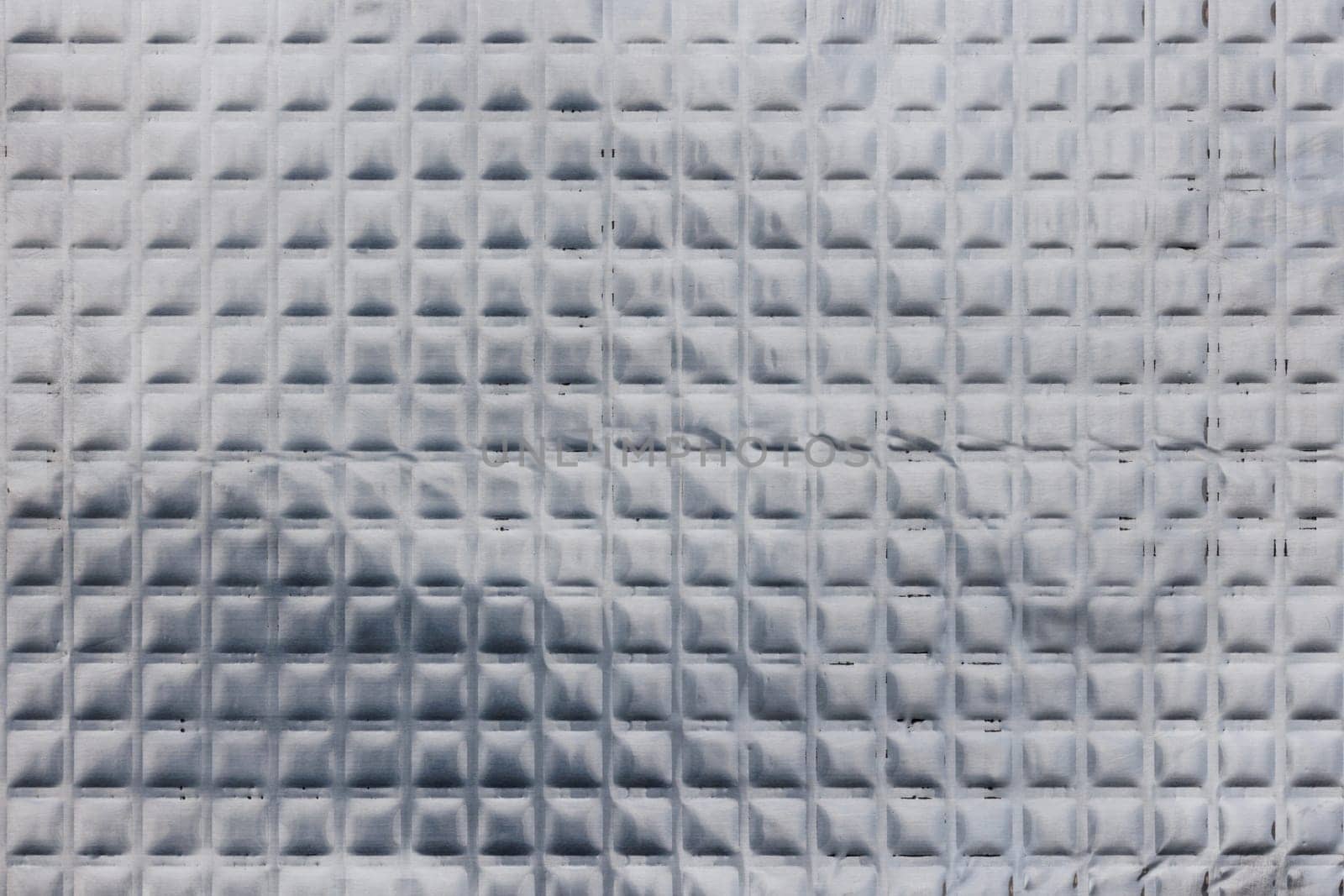 Full-frame texture of aluminum coated butil rubber sheet with square pattern. This material is used for sound dampening in car interiors and vibration resonance reducing and acoustic improving.