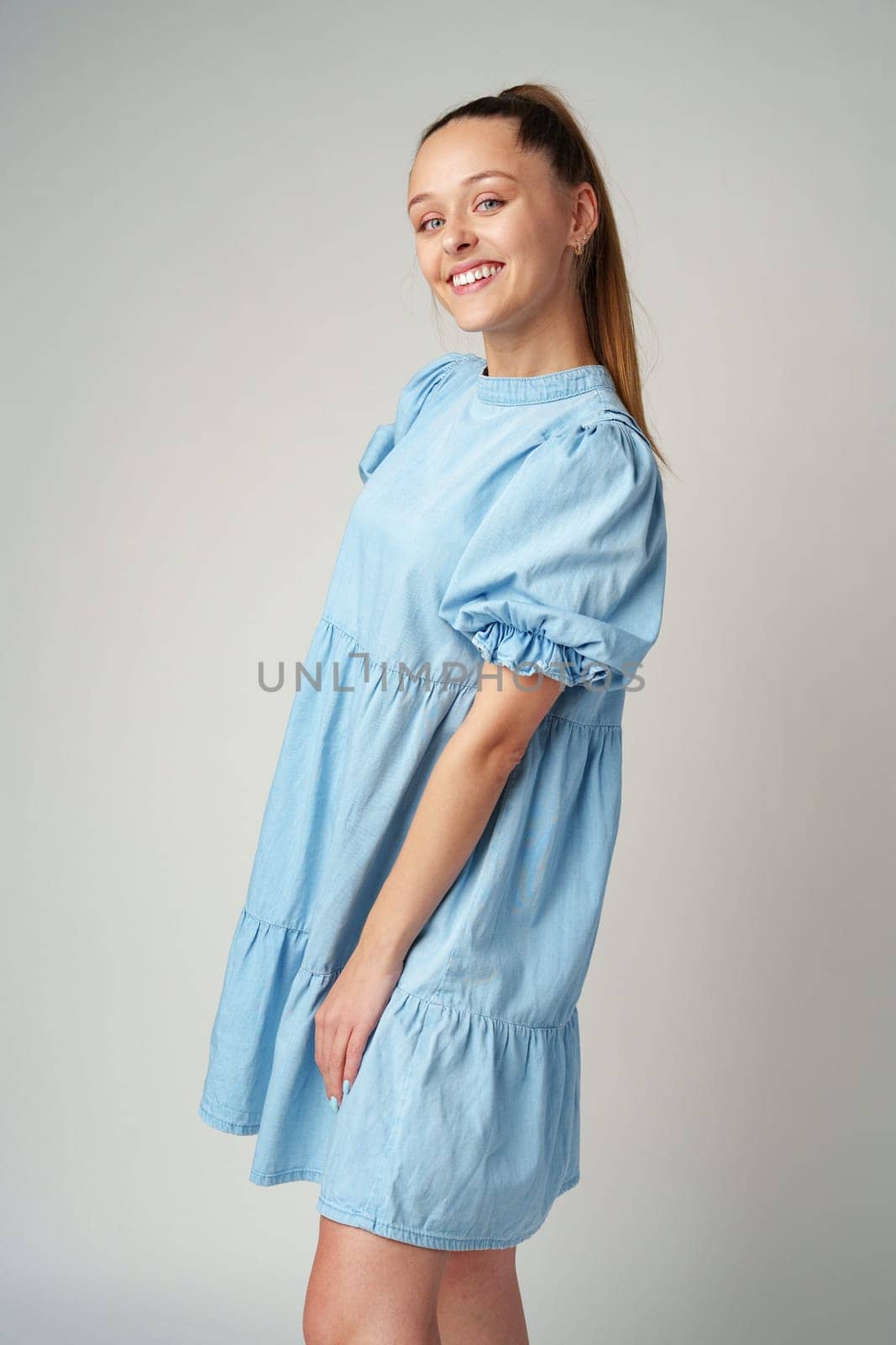 Young happy smiling woman in a light blue dress on a gray background close up