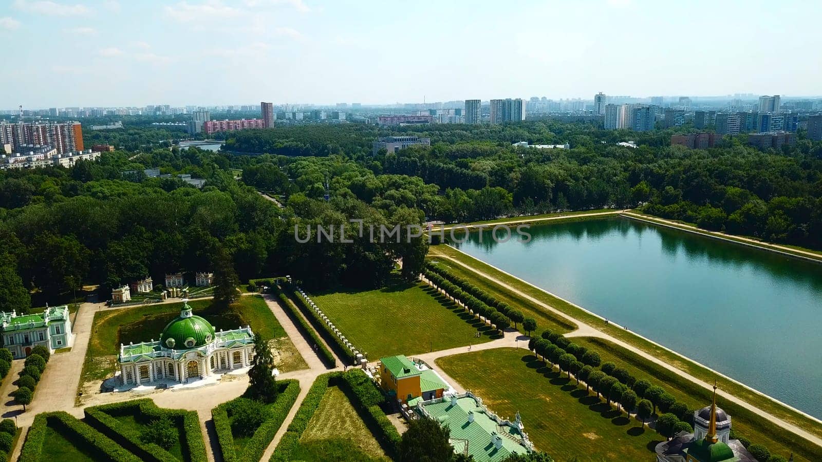 Palace with pond on background of modern city. Creative. Top view of beautiful historical complex on sunny summer day. Palatial buildings with garden and pond with contrast of modern city on horizon by Mediawhalestock
