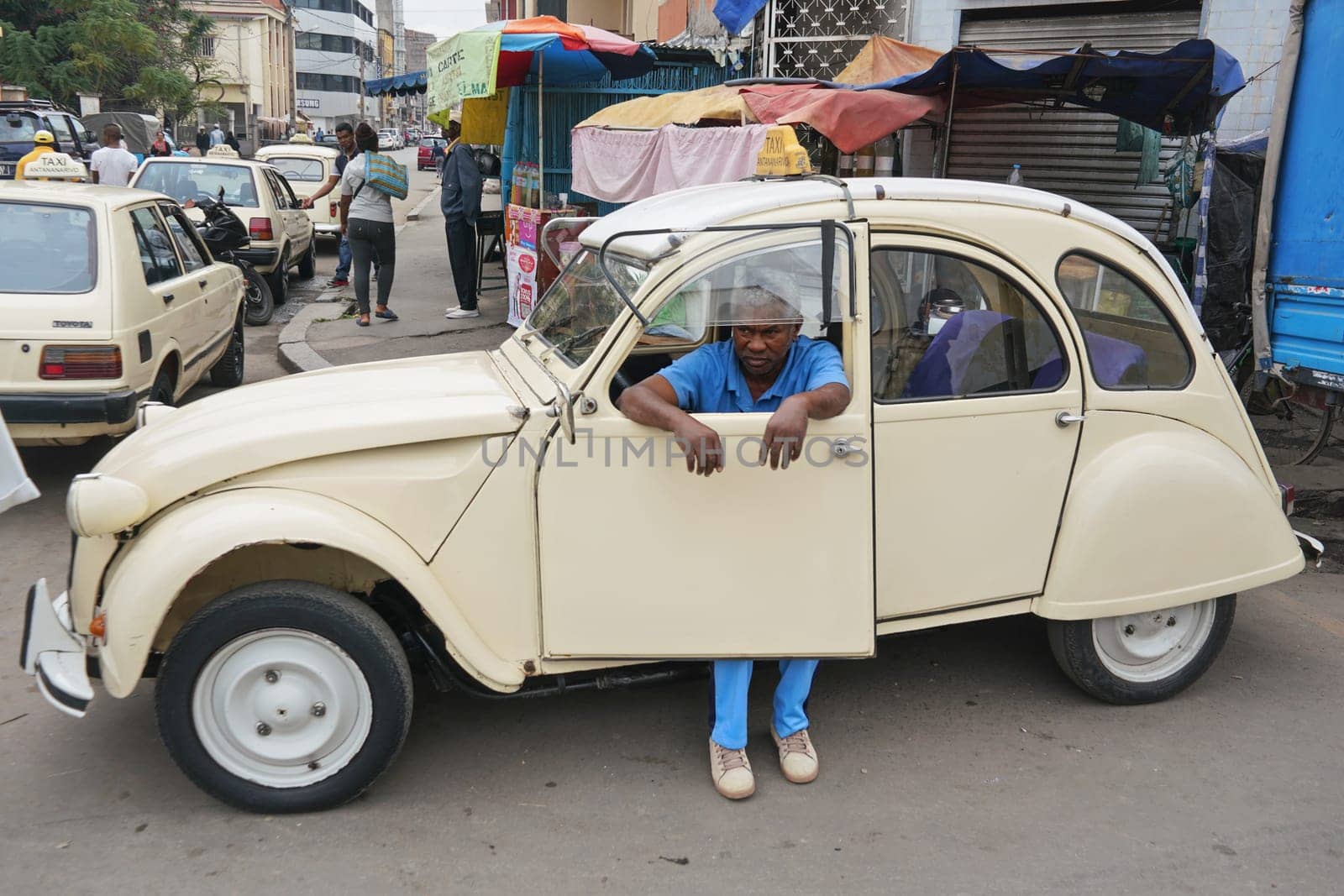 Antananarivo, Madagascar - April 24, 2019: Unknown Malagasy taxi driver resting in his white car on busy main street. People are poor, cars are quite worn, even in Madagascar capital