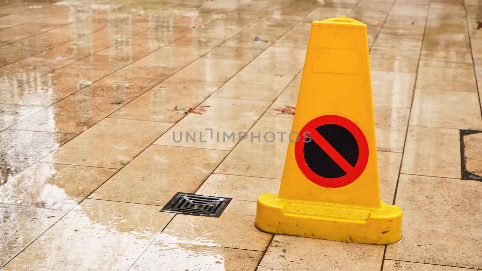 Yellow plastic cone with warning sign on slippery wet tile floor