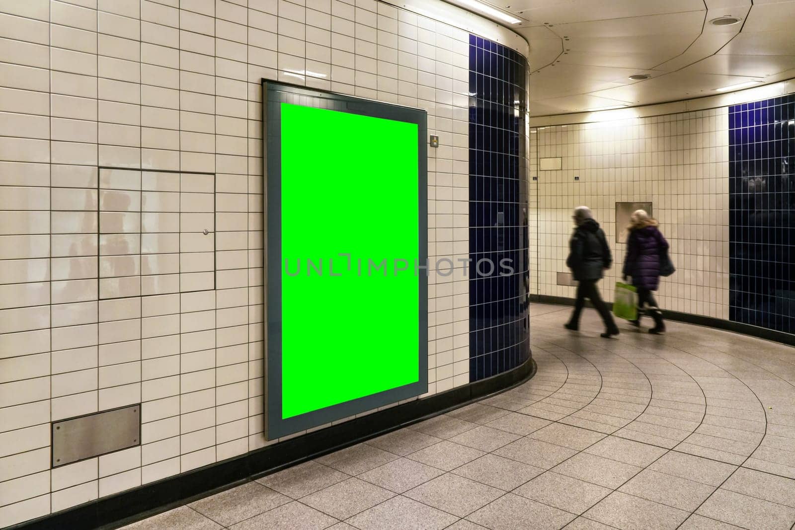 Advertising board display green mockup on wall with white tiles at underground station passage, blurred people in background by Ivanko