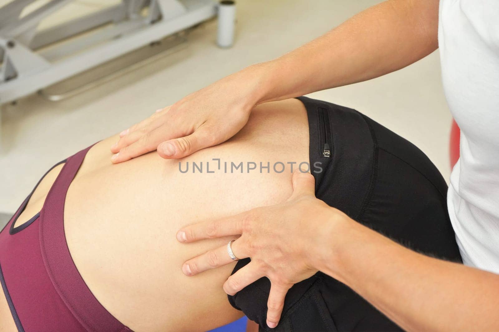 Female physiotherapist examining or exercising back of her patient who is bent forward. Detail on hands over skin