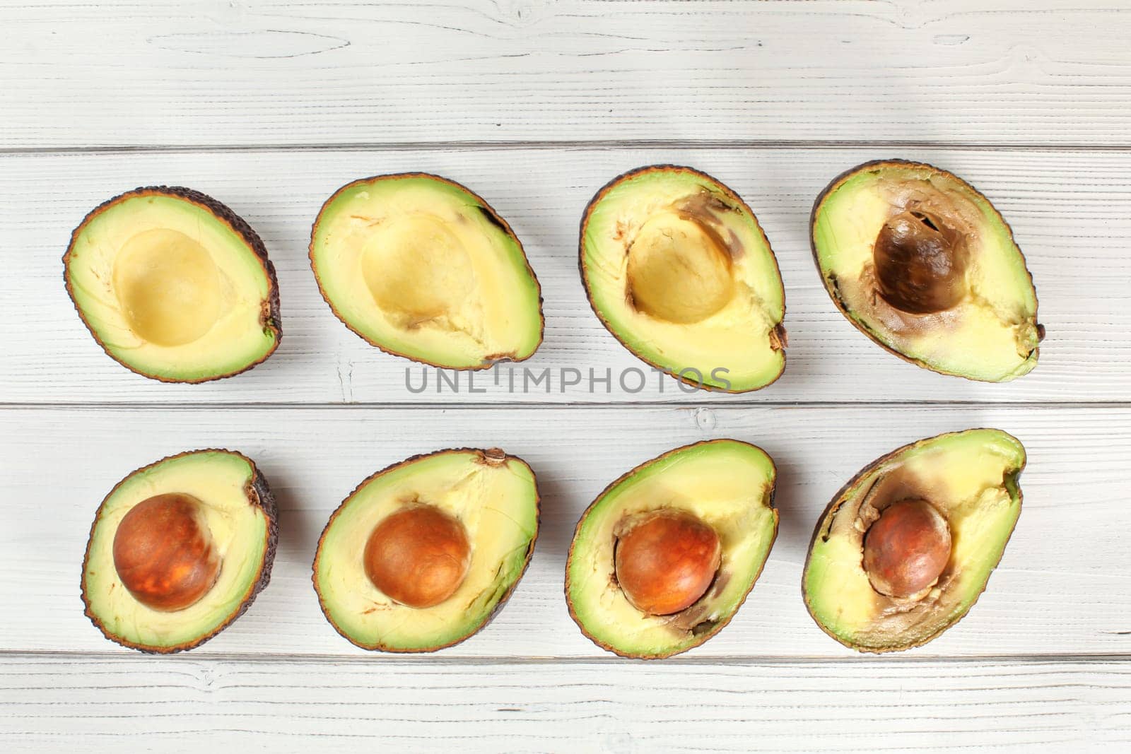 Avocado halves arranged from ripe to over ripen on white boards desk, view from above